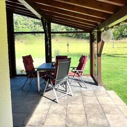 Une terrasse confortable avec une table à manger et quatre chaises. En arrière-plan, une pelouse verte est visible.