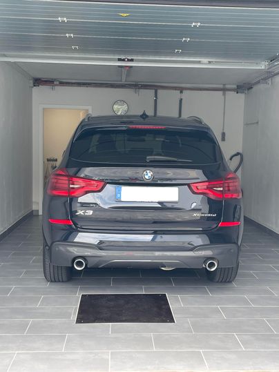 Ein schwarzer BMW X3 steht in einer modernen Garage. Der Boden ist mit hellen Fliesen ausgelegt und eine Uhr hängt an der Wand.