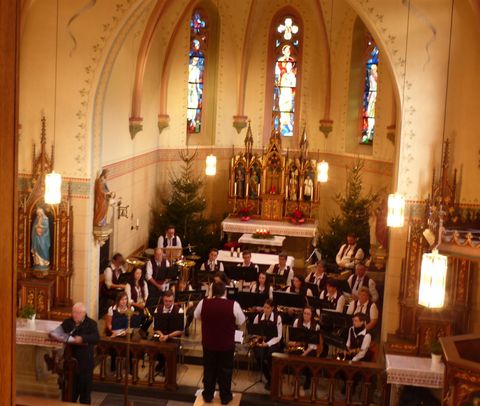A choir is singing in a festively decorated church. In the background, there are Christmas trees and colorful windows.