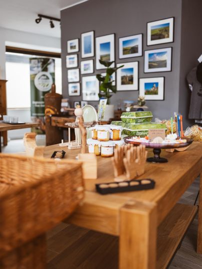 Eine Ladenauslage mit Marmeladengläsern, Geschenkkartons und Bildern an der Wand. Ein Holztisch ist mit verschiedenen Produkten beladen.