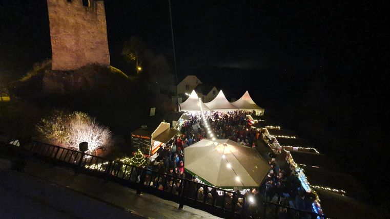 Un événement festif de nuit avec beaucoup de gens. En arrière-plan, on peut voir une ancienne ruine de château.