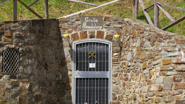 An entrance to an old stone mine. The door is equipped with a grate and above it is the name of the mine.