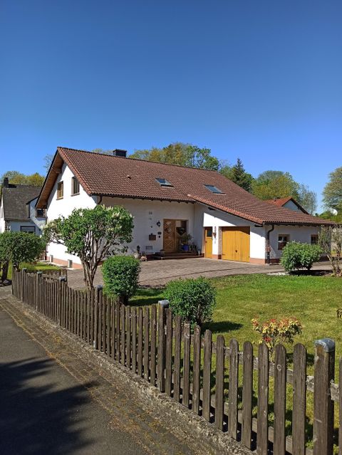 Une belle maison individuelle avec un jardin bien entretenu. Le ciel est bleu et il y a une clôture en bois autour de la propriété.