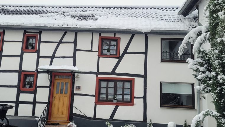 Ein charmantes Fachwerkhaus im Schnee mit einem klaren Himmel. Der Garten ist mit frischem, weißem Schnee bedeckt.