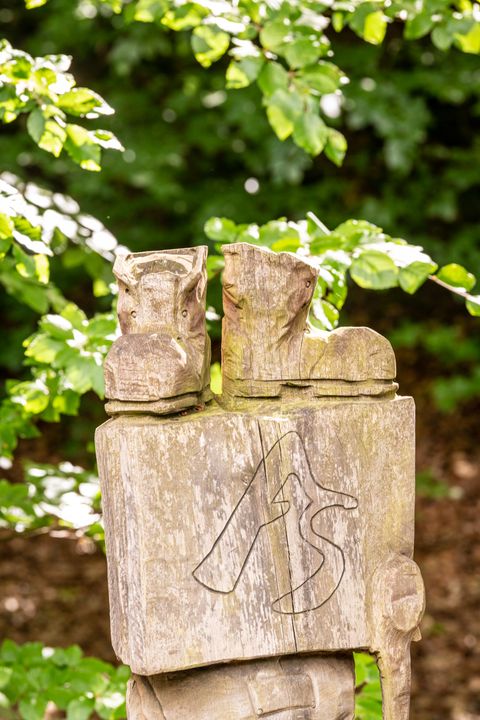 Houten blok met een hoofdletter A en een hoofdletter S voor AhrSteig daarboven staan twee gebeeldhouwde wandelschoenen 
