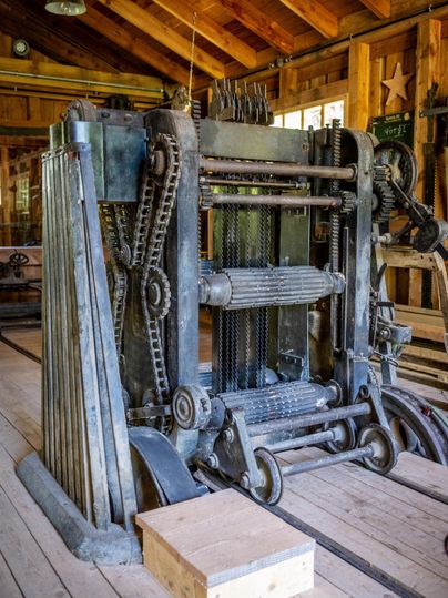 An old printing press stands in a wooden building. It showcases the mechanics and the artisanal design of past times.