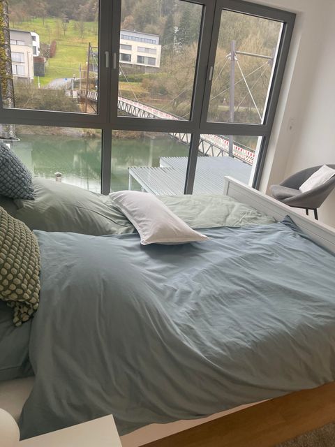 Een gezellige slaapkamer met een groot bed en kleurrijke kussens. Door de grote ramen heeft men uitzicht op het landschap en het water.