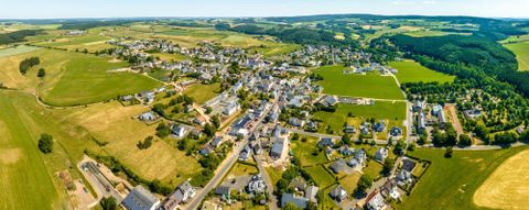 A vast landscape with a small village, surrounded by green fields and hills. The sun is shining and the sky is clear.