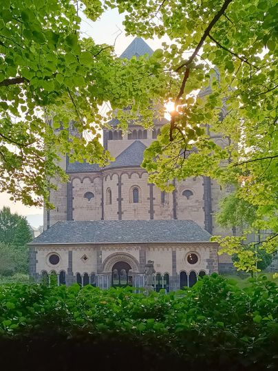 Een indrukwekkende kerk wordt omringd door groene bomen. De zon schijnt door de takken en creëert een rustige sfeer.