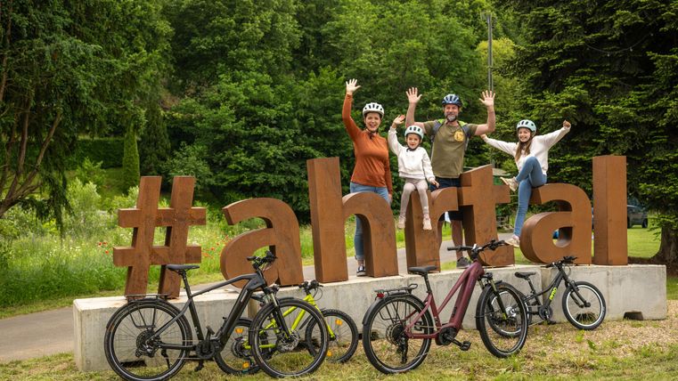 Een gezin staat vrolijk voor een grote #ahrtal opdruk. Op de voorgrond staan verschillende fietsen op een grasveld.