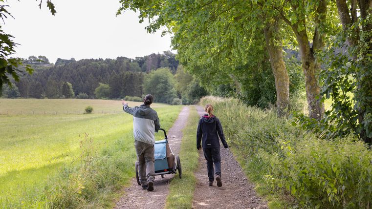 Twee mensen lopen over een landelijk pad omringd door bomen en weilanden.