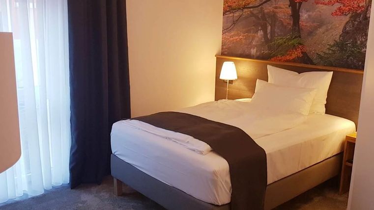 Ein gemütliches Schlafzimmer mit einem Einzelbett und einer modernen Einrichtung. An der Wand hängt ein Bild von einem Baum in herbstlichen Farben.