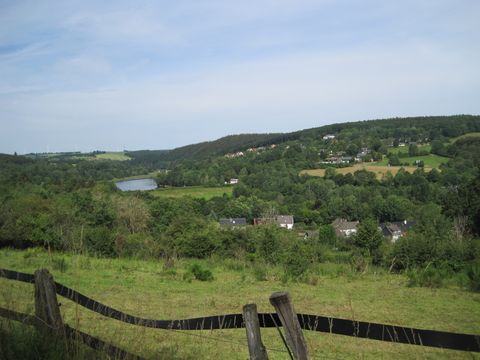 View of Lake Kronenburg in a green landscape with hills and wind turbines in the background.