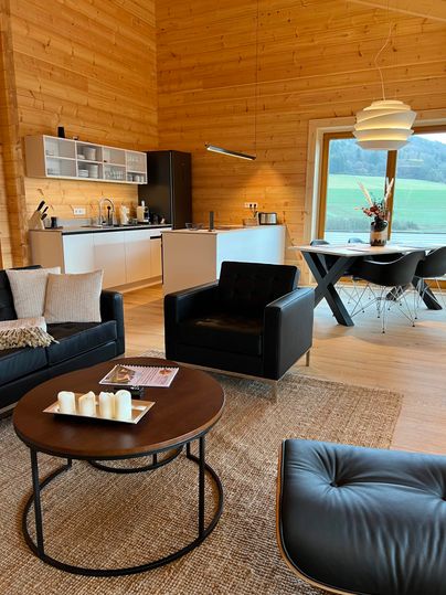 Ein modernes Wohnzimmer mit Holzdecke und großen Fenstern. Die Einrichtung ist stilvoll mit bequemen Möbeln und einem runden Tisch.