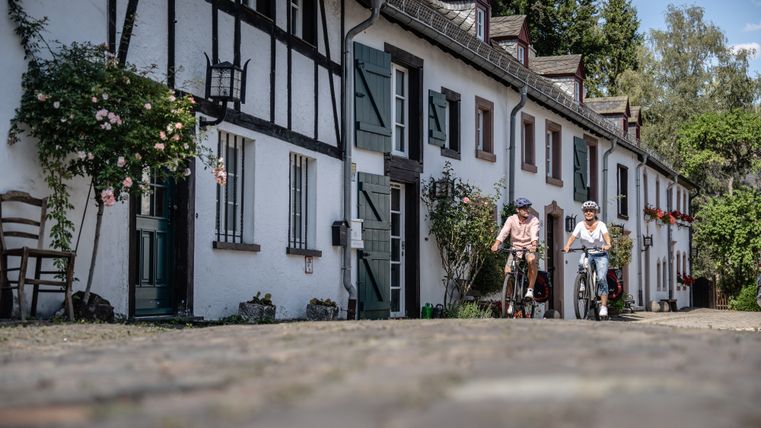 Twee mensen fietsen door een pittoresk, historisch straatje met vakwerkhuizen in Kronenburg.