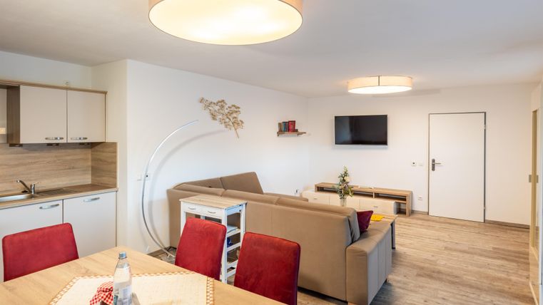 Een moderne woonkamer met een gezellige bank en een eettafel. De muren zijn licht, en er is een televisie en enkele decoratieve elementen.