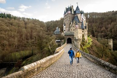 Eine Frau und ein Mann gehen auf einem Weg aus Steinen zur Burg Eltz