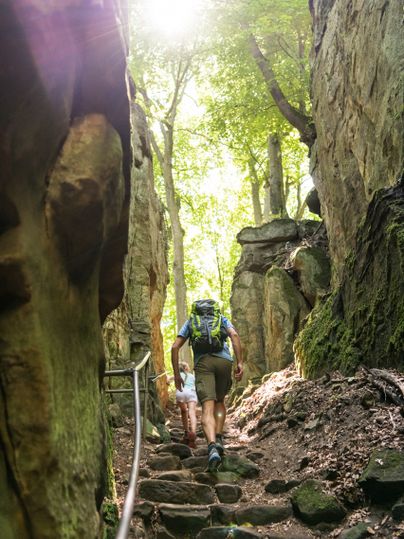 Des personnes se promènent dans une gorge étroite avec des marches en pierre et la lumière du soleil qui brille à travers les arbres.