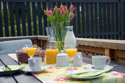Een gedekte tafel in de buitenlucht met verse tulpen en verschillende dranken. Er is sinaasappelsap, melk en kleine snacks op een kleurrijk tafelkleed.