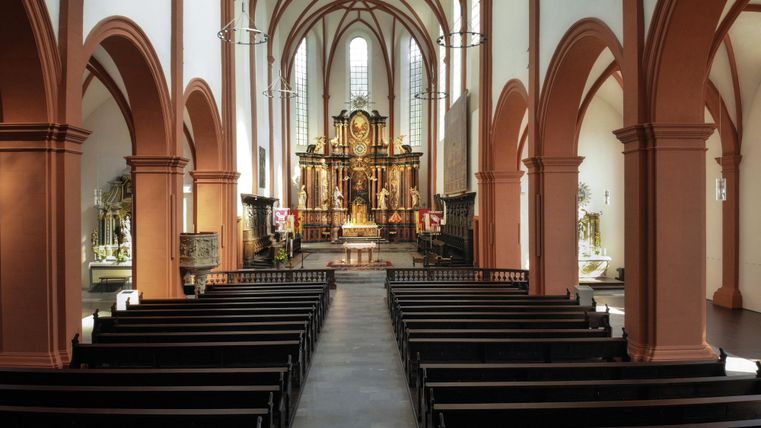 Eine hohe Kirche mit dekorativen Bögen und Holzbankreihen. Der Altar im Hintergrund ist kunstvoll gestaltet.