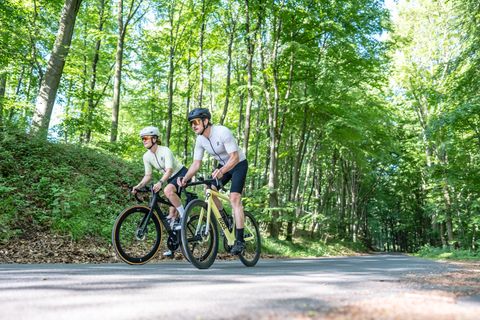 Two racing cyclists on a road in the forest.
