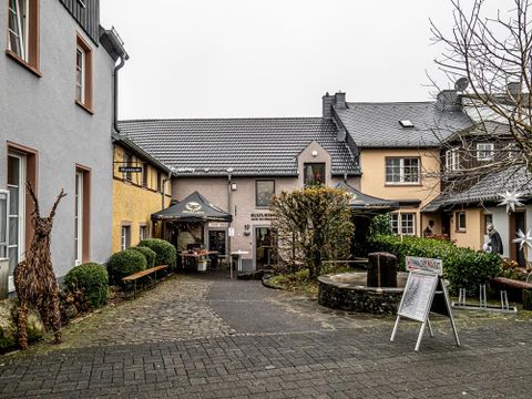 Eine gemütliche Hofsituation mit zwei Gebäuden und einem kleinen Innenhof. Es gibt Sitzplätze im Freien und ein Schilder zeigt verfügbare Dienstleistungen an.