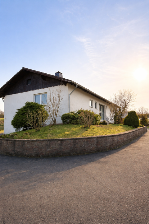 Une maison individuelle moderne avec un jardin bien entretenu et un chemin asphalté. Le ciel est clair et le soleil brille.