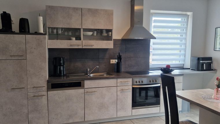 Une cuisine moderne avec des armoires grises et des appareils en acier inoxydable. La pièce est lumineuse et accueillante, avec une table à manger et une grande fenêtre ensoleillée.