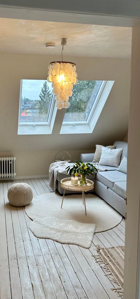 Een gezellige ruimte met een lichte bank en grote ramen. Het lichtspel van de plafondlamp creëert een uitnodigende sfeer.