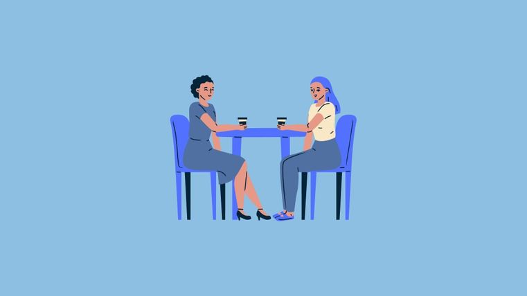 Zwei Frauen sitzen an einem Tisch und halten Tassen mit Getränken. Sie scheinen ein angenehmes Gespräch zu führen.