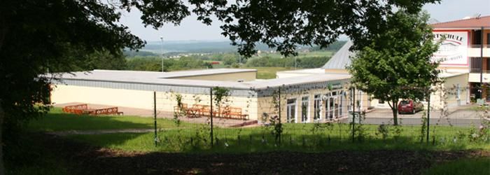 A modern building, surrounded by trees and a wide view of the landscape. The terrace invites you to linger.