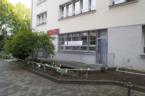Un bâtiment avec une fenêtre entourée d'une grille. Au premier plan, on voit des plantes et un chemin pavé.