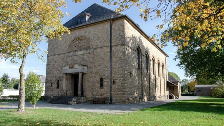 St Hubertuskerk in Wolsfeld, omringd door bomen in de herfst.