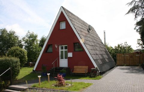 Een rood, driehoekig vakantiehuis met een schuin dak. Omgeven door een groene tuin en een terras.