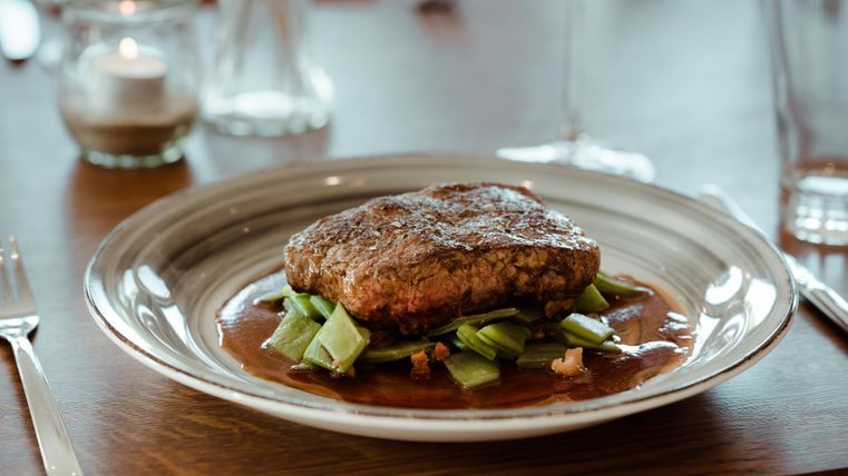 Ein saftiges Stück Fleisch auf einem Bett aus Gemüse. Der Teller ist elegant angerichtet und vermittelt einen gehobenen Eindruck.
