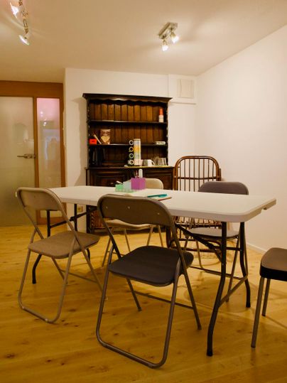 Une pièce simple avec une table et plusieurs chaises. À l'arrière-plan se trouve une armoire antique.