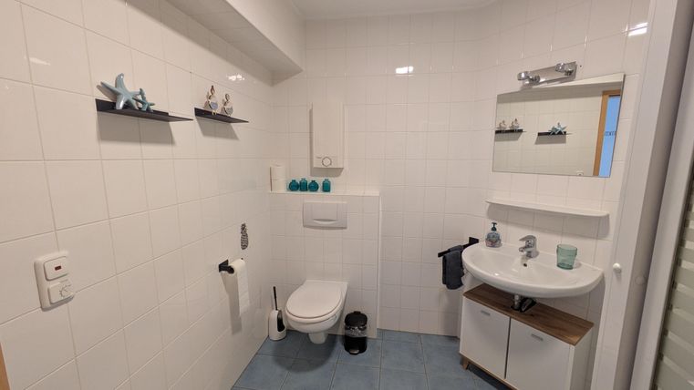 Een moderne badkamer met witte tegels en blauwe accenten. Het heeft een toilet, een wastafel en planken met decoratieve elementen.