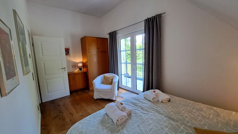 Ein einladendes Schlafzimmer mit einem großen Fenster und Zugang zu einem Balkon. Die Einrichtung ist modern und gemütlich, mit hellen Farben und einem bequemen Sessel.