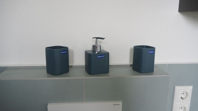 Drei dekorative Badezimmerbehälter in einem modernen Design. Sie stehen auf einer Ablage und sind in verschiedenen Formen und Größen.