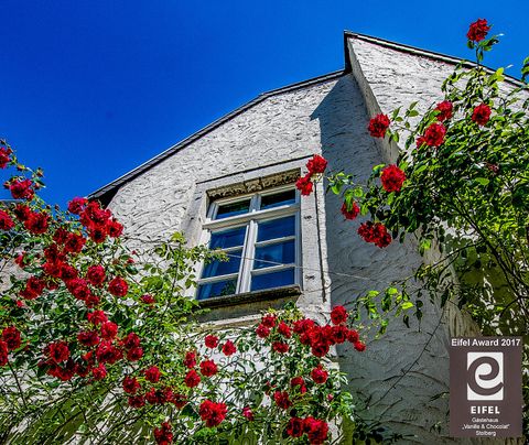 Une maison charmante avec un crépi blanc et une belle fenêtre. Des roses rouges entourent la façade et le ciel est d'un bleu éclatant.