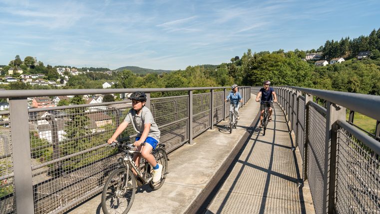 Familie fährt mit Fahrrädern über eine Brücke auf dem Maare-Mosel-Radweg.