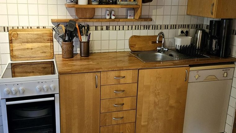 Een moderne keuken met houten afwerkingen en witte tegels. Er is een fornuis, een gootsteen en een vaatwasser.