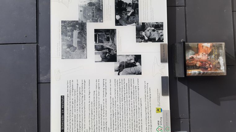 Eine Informationstafel mit historischen Fotos und Text. Die Bilder zeigen Szenen aus der Vergangenheit, umgeben von einer klaren Präsentation.