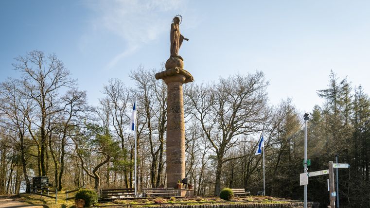Colonne de Marie près de Waxweiler avec un ciel bleu et des arbres en arrière-plan.