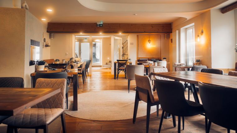 A modern restaurant with wooden floors and stylish tables. There are large windows that let in light and a welcoming atmosphere.