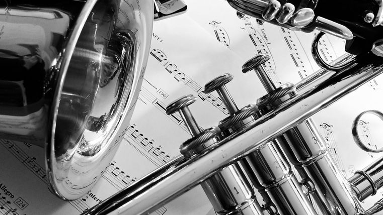 Eine Ansammlung von Musikinstrumenten, darunter eine Klarinette und Trompeten, liegt auf Notenblättern. Die Szene ist in Schwarz-Weiß gehalten.