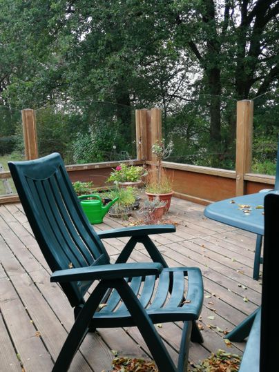 Een gezellige balkon met een blauwe stoel en een tafel.
Plantenbakken en groene planten geven de ruimte een uitnodigende sfeer.