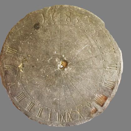Une ancienne horloge solaire en pierre avec des chiffres romains et un design simple. L'horloge indique les lignes horaires et a une ouverture centrale pour le gnomon.