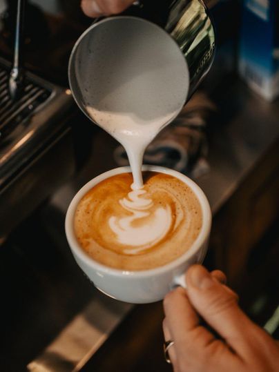 Een persoon giet stoomafgevende melkschuim in een kopje koffie. De kunstzinnige latte-art is duidelijk zichtbaar.