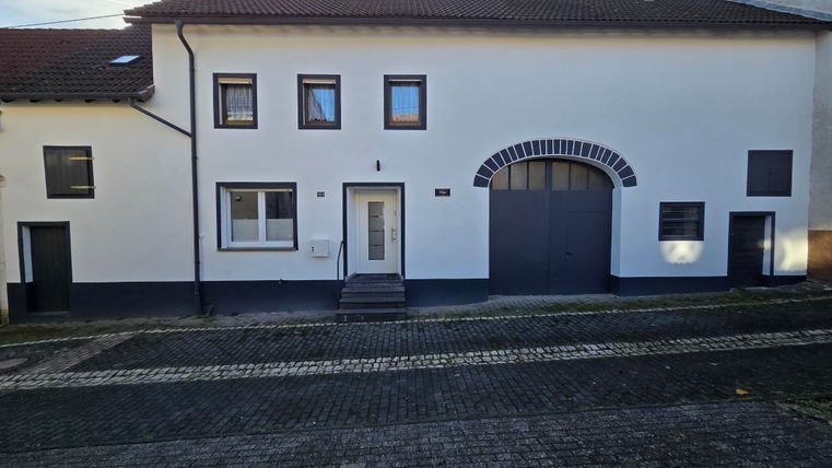 Une maison moderne avec une façade blanche et plusieurs fenêtres. La porte d'entrée est bien visible et un grand portail est également présent.